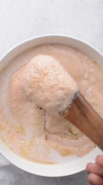 Overhead of moi moi mixture in a white ceramic bowl, top view of nigerian bean pudding being mixed, process of making nigerian moi moi