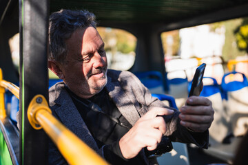 Senior man using smartphone on city tour bus © Nazareno