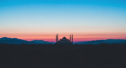 Silhouette of a mosque against a vibrant sunset sky with distant mountains.