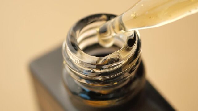 Close up of golden serum dripping from pipette into glass bottle with flecks of gold
