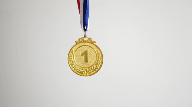 Shiny gold first place medal hanging on tri color ribbon against white background with subtle motion