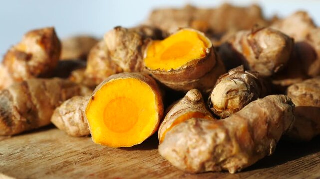 Fresh turmeric roots with cut slices on wooden table in bright natural light