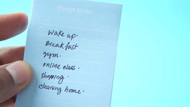 Hand holding blue to do list with tasks like wake up and breakfast