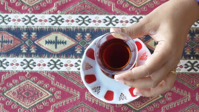 Woman's hand taking away glass of traditional turkish tea from a table with a patterned red tablecloth