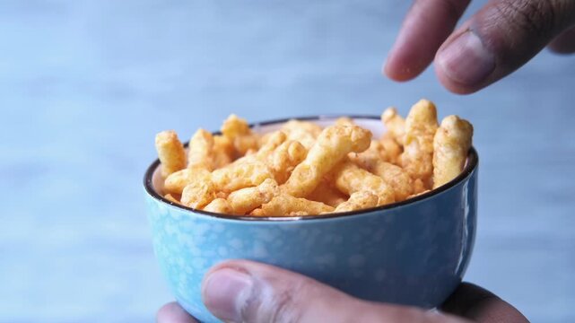Person taking crunchy corn puffs from bowl in slow motion footage of delicious salty snacks being picked by hand