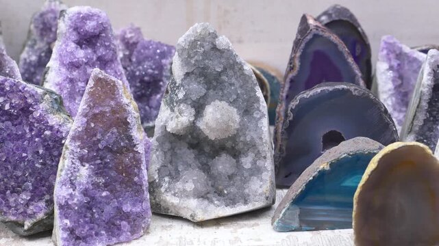 Natural amethyst geodes and colorful agate crystals displayed on white wooden surface in close up panning motion