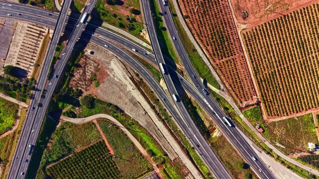 Vehicles move along multiple highways surrounded by fields and vineyards in a rural setting during daytime under clear skies.
