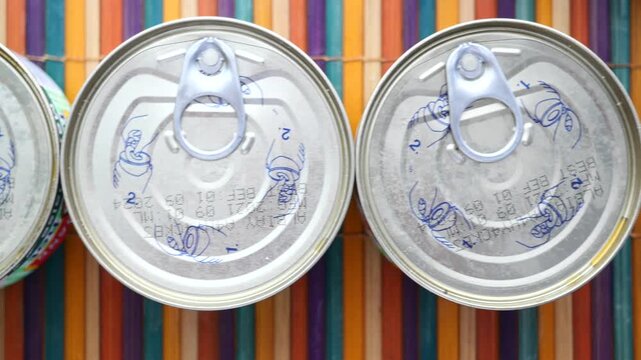 A top-down dynamic clip showing multiple sealed metal canned food items with easy-open lids moving across a colorful striped background