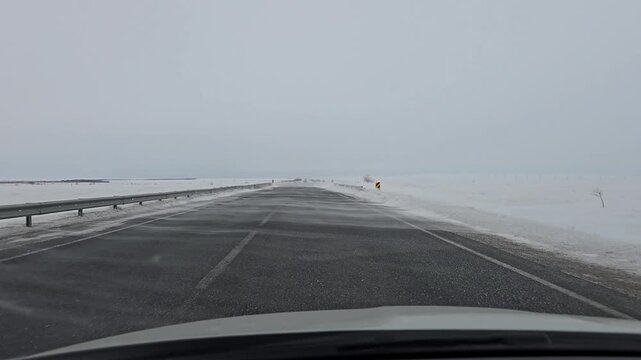 A view from a car onto a snow-covered road during strong winds and snowdrifts in the steppe of Kazakhstan.