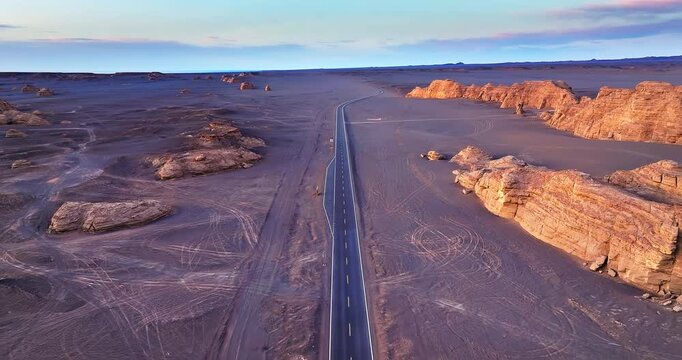 Aerial view of a long empty asphalt highway through the vast Yardang landforms and Gobi desert in Xinjiang, China.