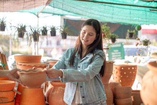 Young Woman Standing and Reaching Up to Touch a Hanging Potted Plant