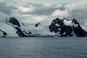 Glimpse of icy mountains and glaciers along the coast of Antarctica on an overcast day with dark clouds overhead © ANITEK MEDIA 