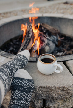 A woman sitting by a fire with a cup of coffee .