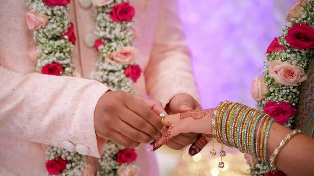Close up view of Indian bride and groom exchanging rings during a traditional wedding ceremony. hands with floral garlands and elegant cultural attire during engagement ritual.