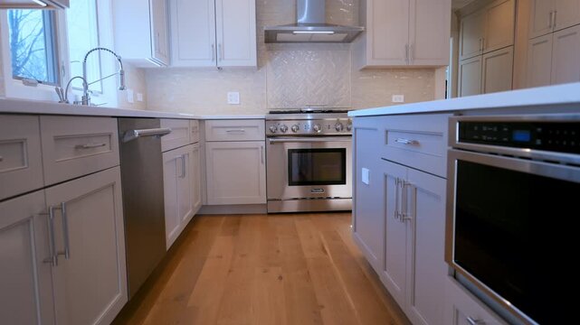 Modern residential kitchen with white cabinets, stainless steel oven, range hood, and wooden floor. Bright contemporary home interior design.