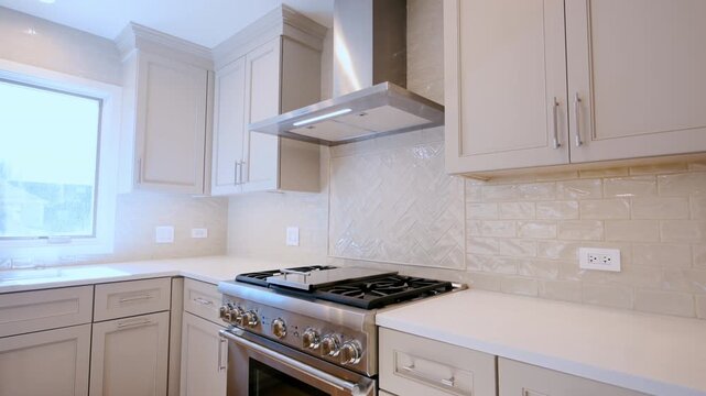Wide view of Modern kitchen interior with stainless steel range hood, white cabinets, and tiled backsplash. Clean contemporary residential design detail.