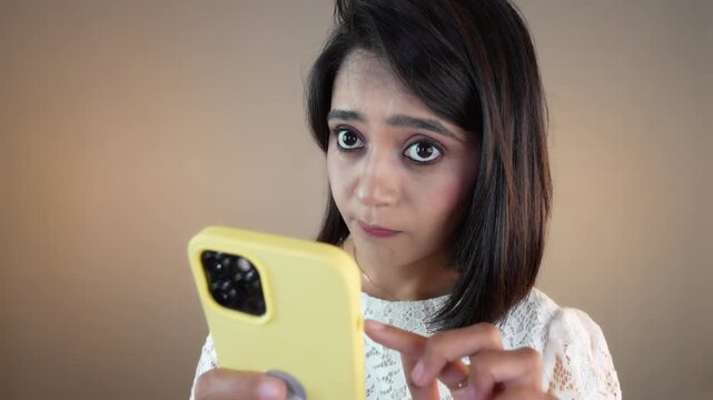 Close up of sad unhappy young Asian girl woman student using smart phone typing sms chat online look at camera, isolated over grey studio background.