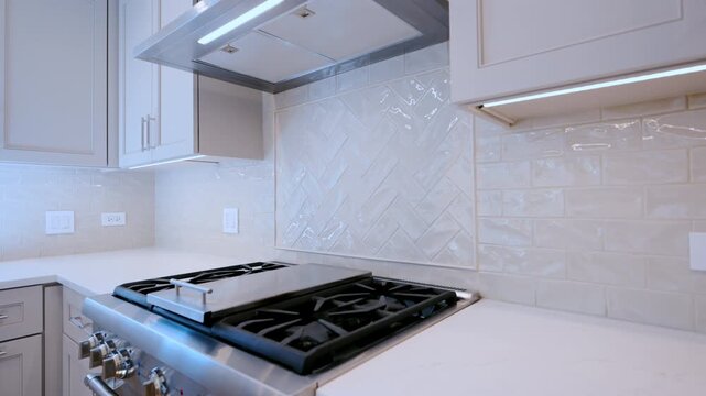 Modern kitchen interior with stainless steel range hood, white cabinets, and tiled backsplash. 