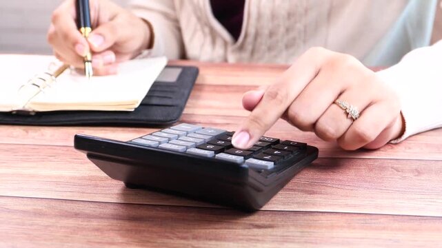 Businesswoman calculates finances with calculator and takes notes on notebook at wooden table business and finance concept slow motion clip