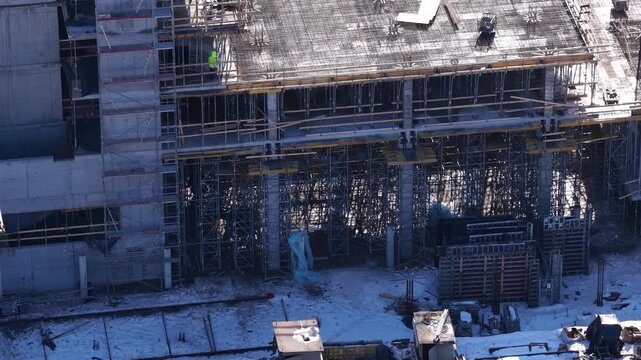 Aerial drone view of an active construction site with tower crane, reinforced concrete framework, workers, and building structure under development during winter in Vilnius, Lithuania.