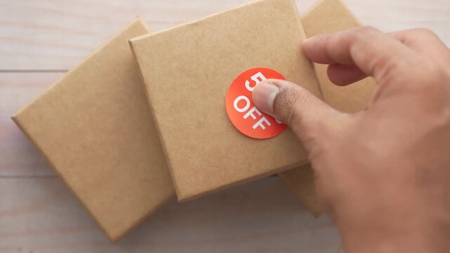Hand applies 50% off sticker onto brown gift box for sale promotion