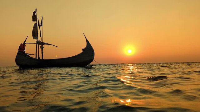 ​Traditional Wooden Vessel Sailing on Calm Sea Waves During Vibrant Tropical Sunset at cox's bazar