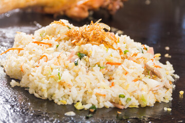 A serving of fried rice with vegetables and shredded meat placed on a hot iron plate