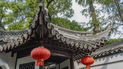 Chinese architecture. Details. Tiled roof with curved cornice edges. Traditional red lanterns are suspended. Carved wooden decorative elements. Trees against the sky. China. Shanghai © Вера 