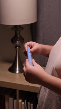A vertical medium shot of a young woman screws a needle on pre-filled pen injector to prepare it for taking medicine