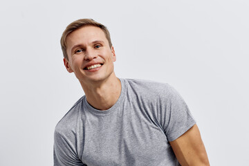 Fototapeta premium Smiling young man with short light brown hair and bright expression, wearing casual grey t-shirt, looking at camera, isolated on plain white background, studio portrait. People lifestyle concept