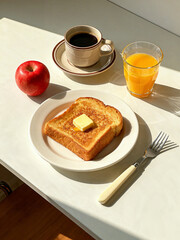 Breakfast set with butter toast, fresh red apple, orange juice, and black coffee on a white table