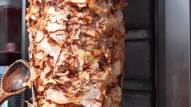 Man slicing meat from a vertical rotisserie preparing shawarma for serving