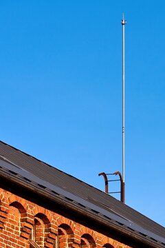 Lightning rod on roof of historic red brick building against clear blue sky. Architectural detail of lightning protection system on traditional European architecture with copy space.