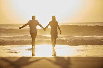 Fototapeta premium Back, couple and holding hands for travel at beach with love, adventure and bonding on holiday. Space, people and walking in sea water with partner, explore nature and sunset sky on getaway vacation