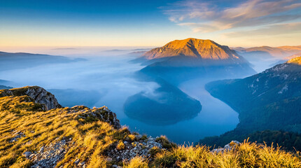 Naklejka premium Breathtaking panoramic view of a serene horseshoe lake enveloped in mist, with a golden-lit mountain peak rising above.