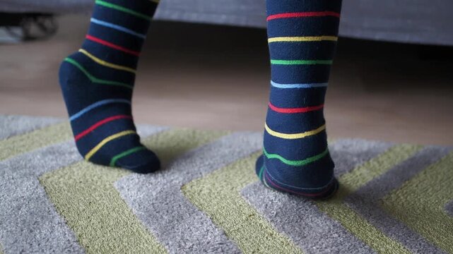 Person wearing colorful striped socks standing on rug, close up on feet moving gently