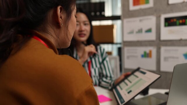Two businesswomen discussing startup ideas and reviewing documents during a meeting in modern office, representing teamwork, business planning and collaboration in a startup company.