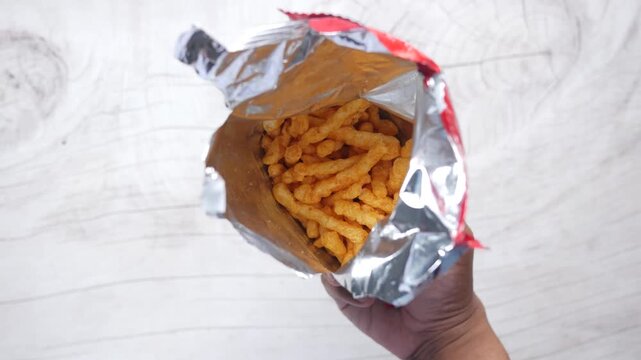 Top view of open bag with spicy corn puff snacks on light wooden surface