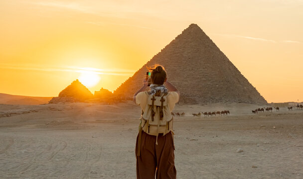 Tourist takes a photo of the pyramids in Egypt during sunset while camels walk in the background