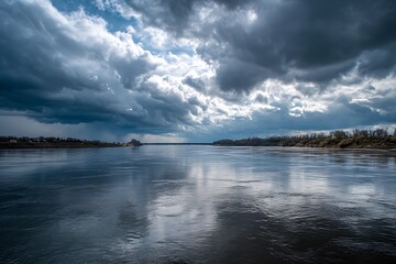 A wide river slowly flowing under a dramatic cloudy sky, creating a calm yet powerful atmosphere