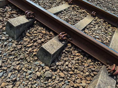rusty steel railway tracks on concrete sleepers and stone ballast in outdoor sunlight