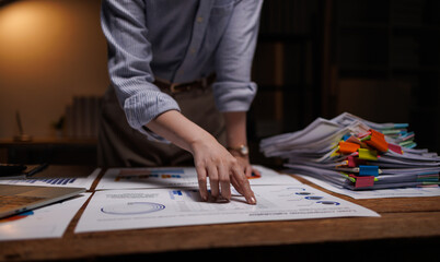 Fototapeta premium Focused Asian businesswoman analyzing financial report graphs while working late at night