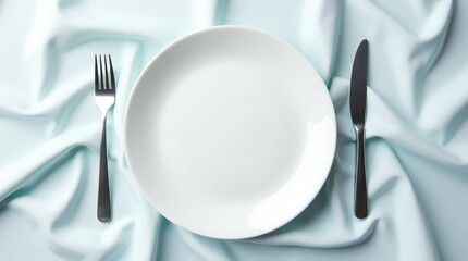 Pristine white ceramic plate with silver fork and knife on light blue fabric table setting