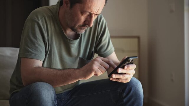 Man sitting on sofa in casual clothes holding smartphone. 4K