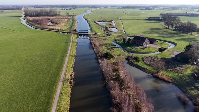 Aerial view of a Dutch polder landscape with a canal, water sluice, and traditional farmstead surrounded by green fields and drainage moats under a clear sky.