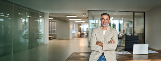Confident happy rich middle aged business man ceo manager, 50 years old team leader, mature professional lawyer, male company executive wearing suit standing arms crossed in office, profile portrait. © insta_photos