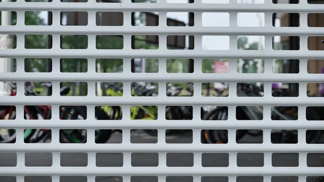White metal security roller shutter with a grid pattern over a closed shop window with blurred bicycles inside.