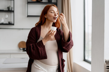 Fototapeta premium Pregnant woman enjoying healthy yogurt snack in kitchen, focusing on nutrition