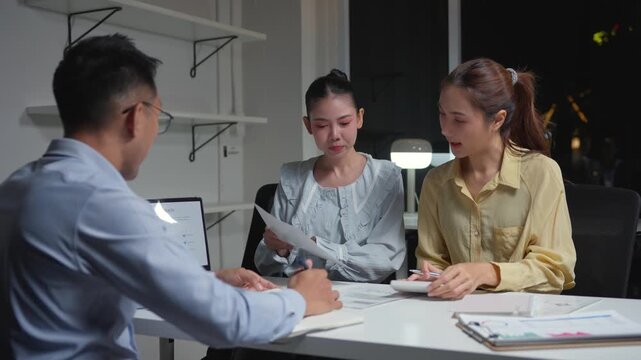 Stressed asian businessman reprimanding his two female colleagues. Overworked team arguing about project results in the office at night