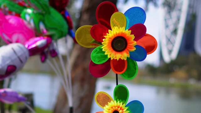 Colorful flower wind spinner rotating near lake with balloons in background